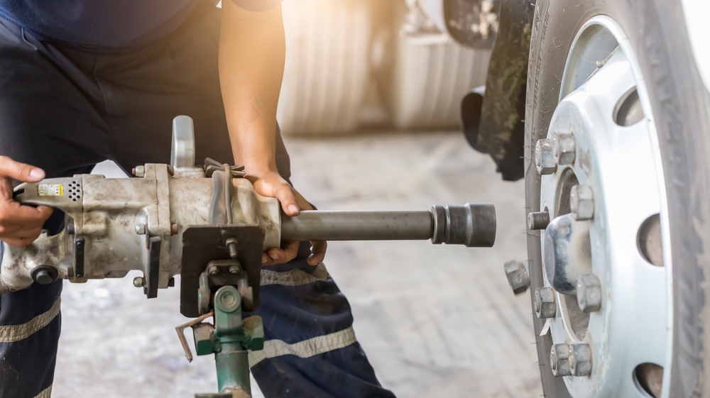 Mechanic,Undoing,Wheel,Nuts,On,Truck,Rotating,Wheels