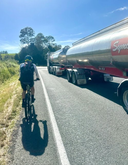 Cyclist,In,Cycleway,On,Left,Of,Road,With,Large,Truck,And,Trailer,Passing.
